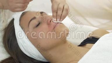 专业美容师用餐巾纸在美容院擦拭女孩的嘴唇。
